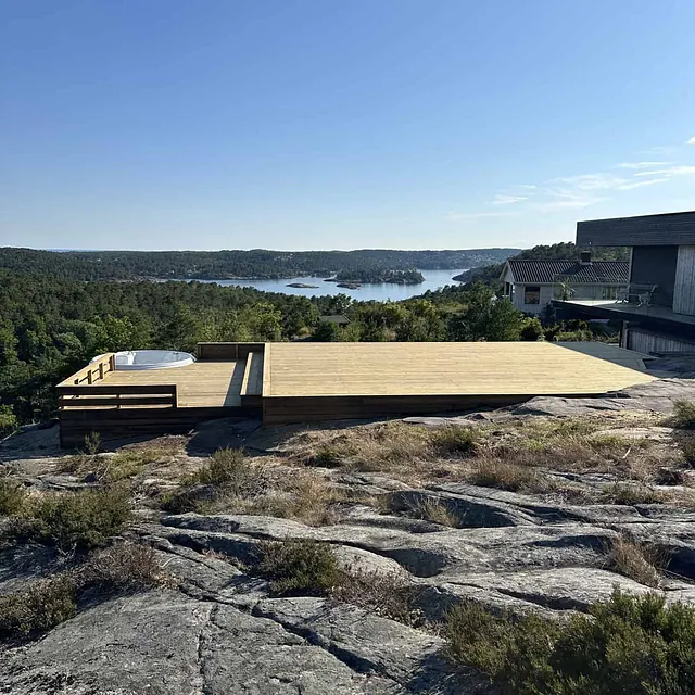 Stor treplatting med boblebad og trapper, foran en skog og et vann.