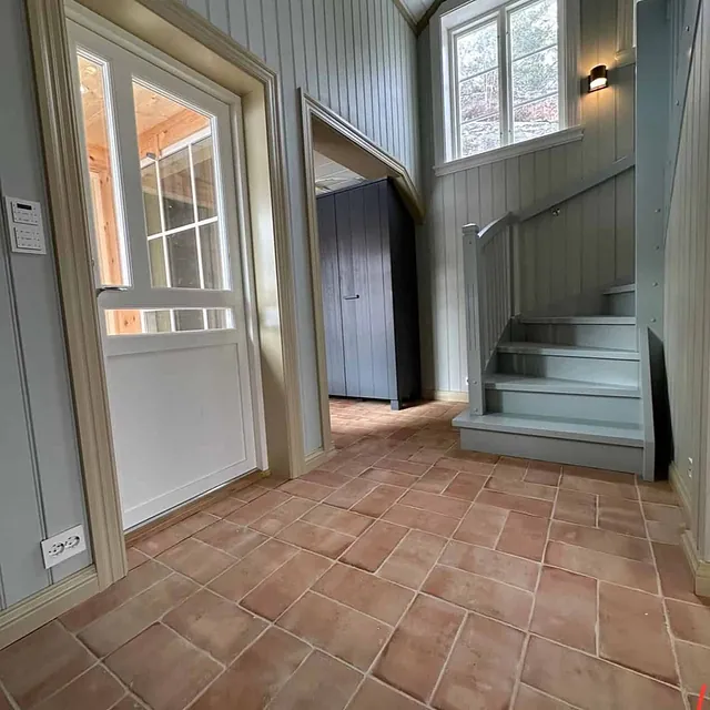 Et inngangsparti med et gulv av terracotta fliser og en trapp.