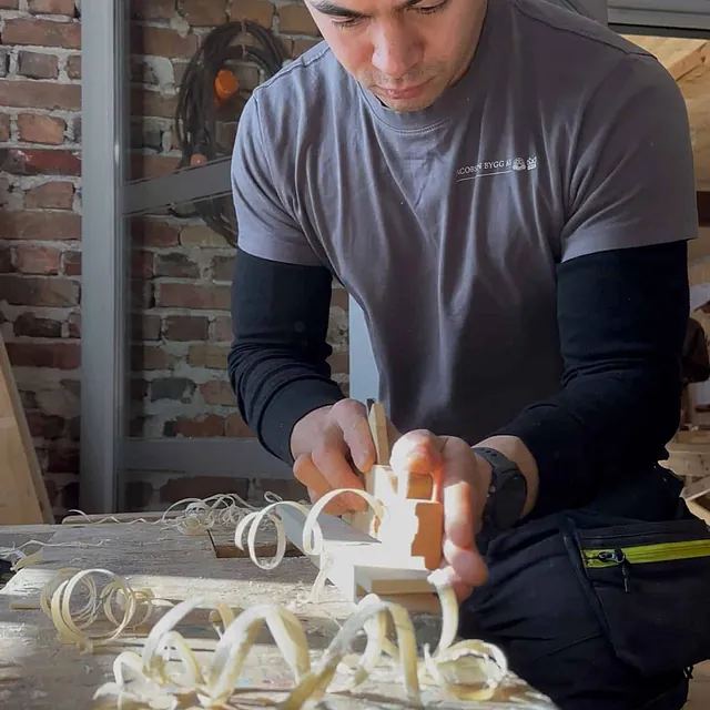 En tømrer som høvler en trekloss i et verksted.