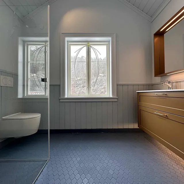 Et bad med trepaneler på veggene, mørkeblått gulv og takvindu.