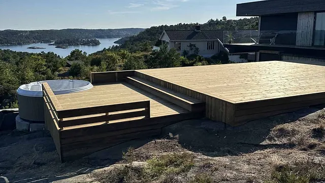 Stor treplatting med boblebad og utsikt over et vann og skog.