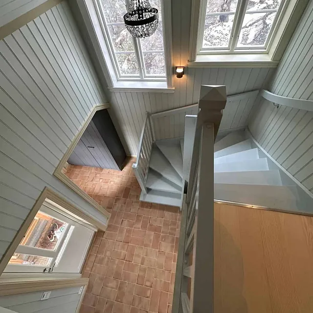 Et rom med et gulv av terracotta fliser, trapp og takvinduer.