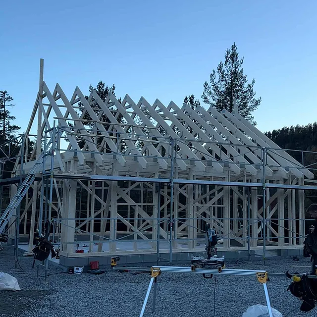 Skjelettet til et hus under bygging med trereisverk, stillas og snekkerverktøy.