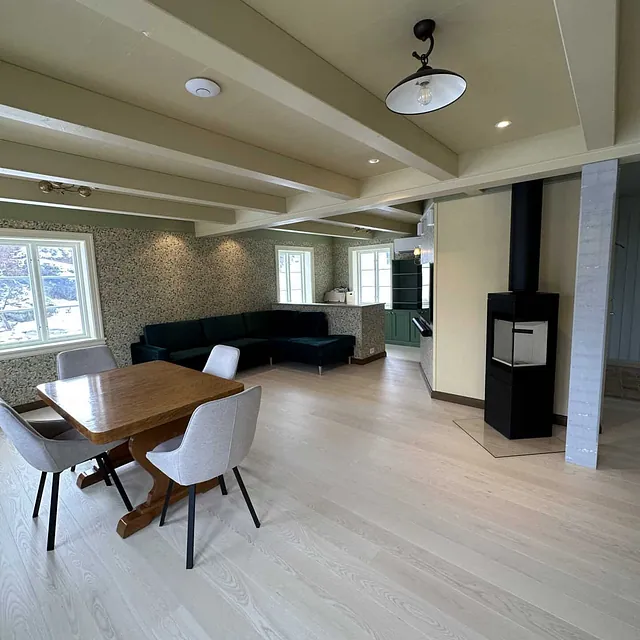 En stue med parkettgulv, spisebord og en peisovn.