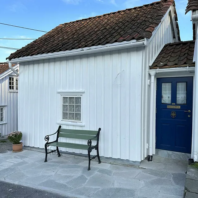 Et lite, hvitmalt hus med en grønn benk og blå dør.