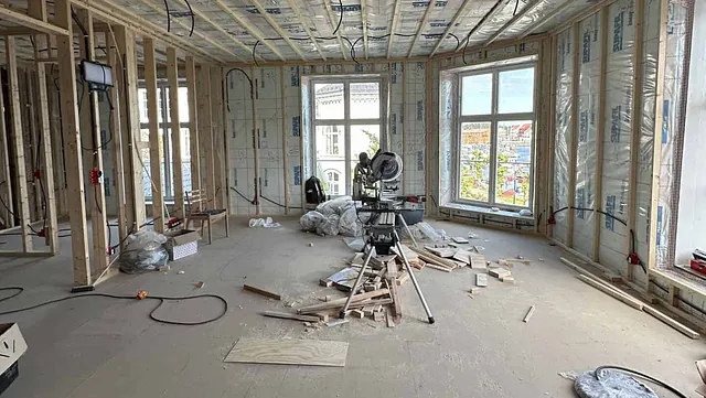 Innsiden av et hus under bygging, med synlige takbjelker, ledninger og verktøy.