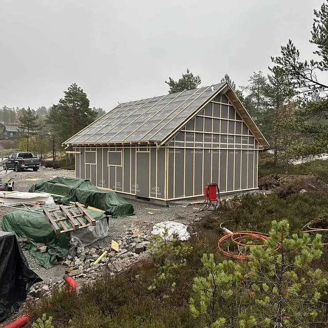Et grått hus under bygging med synlig reisverk og materialer rundt.