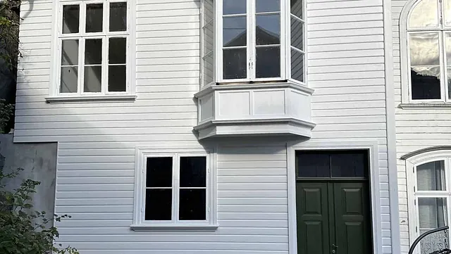 Et hvitt hus under restaurering, med nye vinduer og en mørkegrønn dør.