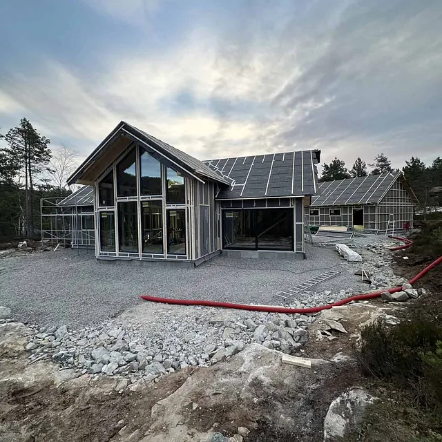 To huskropper med store glassvinduer under bygging, foran en skog.