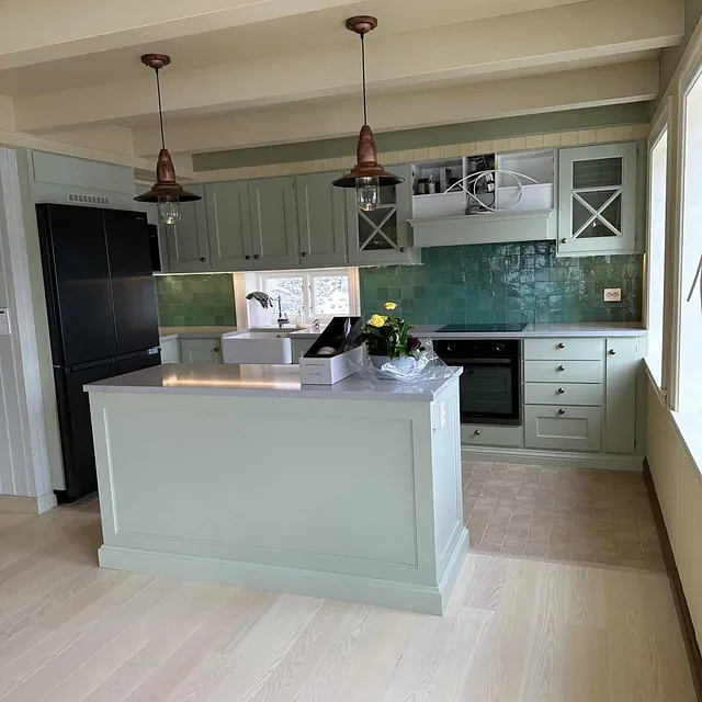 Et kjøkken med en kjøkkenøy, grønne skap og hvite bjelker i taket.