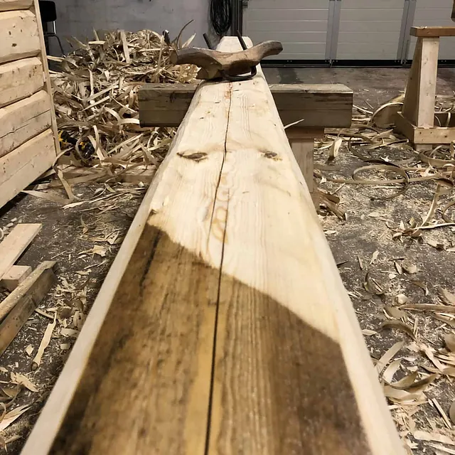 Nærbilde av en trestamme som blir formet til en bjelke, med en stor splitt.