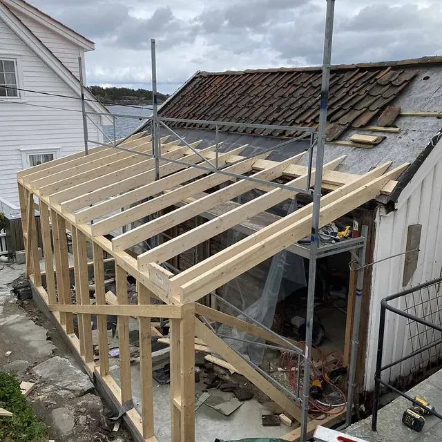 Et reisverk som bygges ved siden av et gammelt hus med takstein.