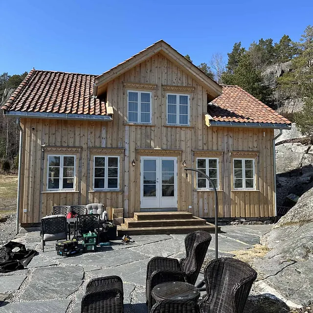 Et nylig kledd hus i treverk med takstein, møbler og verktøy utenfor.