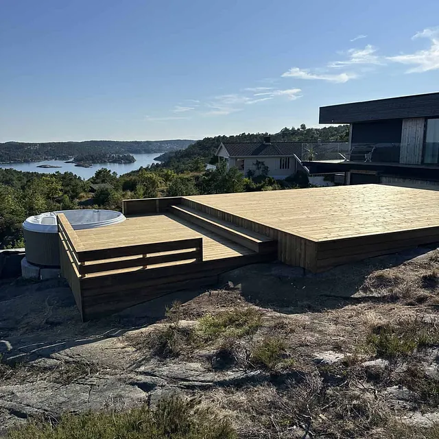 Stor treplatting med boblebad og utsikt over et vann og skog.
