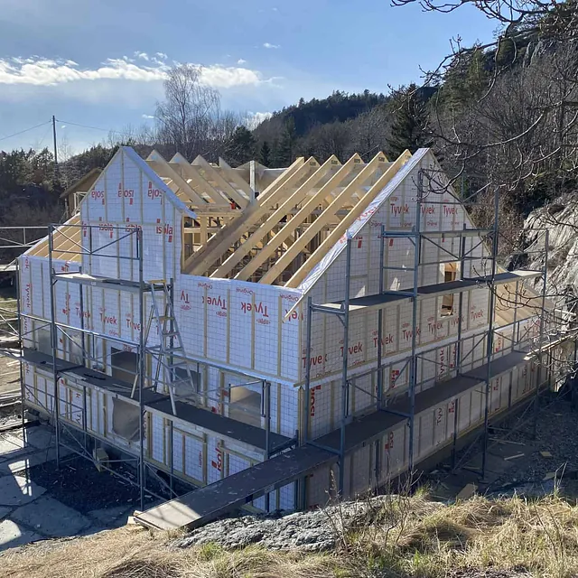 Hus under bygging, innkledd i hvitt byggemateriale med reisverk som er synlig.