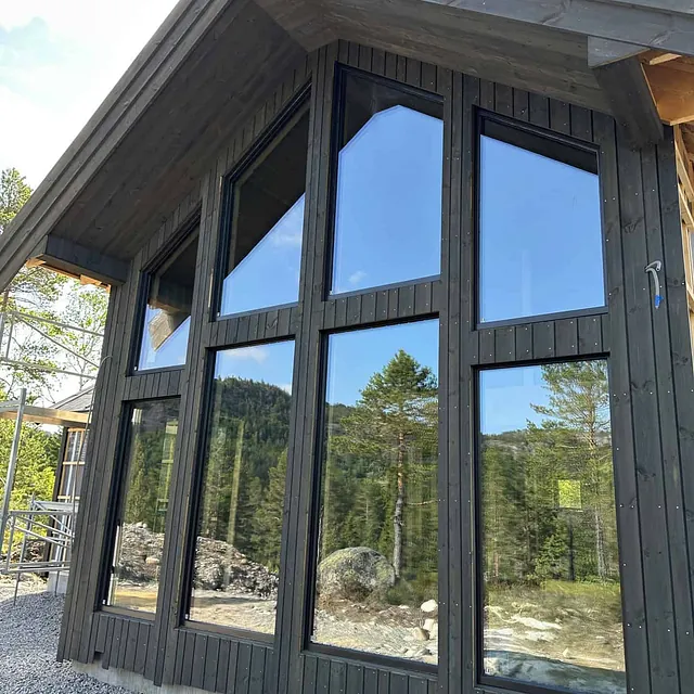 Et hus med store, moderne vinduer som reflekterer skogen rundt.